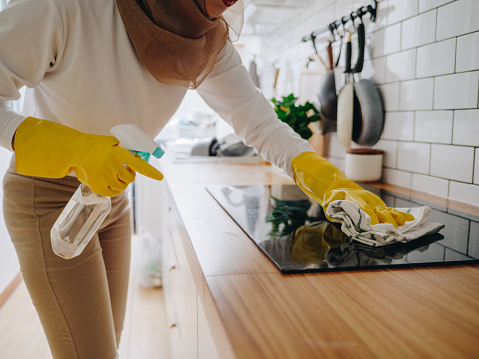 Muslim girl cleaning cooktop cooking panel on kitchen.