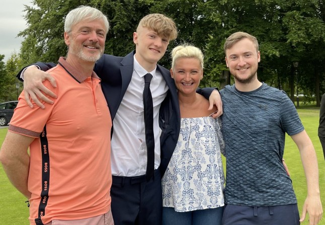 Katie Webster with her husband, Andrew (far left) and two sons, Tom and Fin (either side of Katie), all standing outside on grass with trees in the background (Picture: Katie Webster)