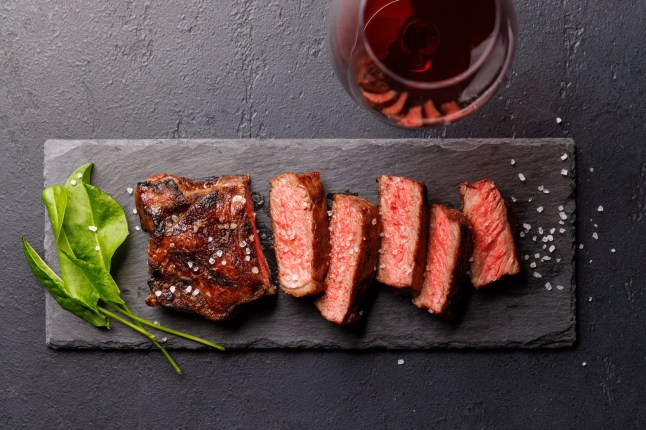 A perfectly cooked sliced striploin steak with a juicy, tender texture on a dark background. A gourmet meal for steak and wine lovers