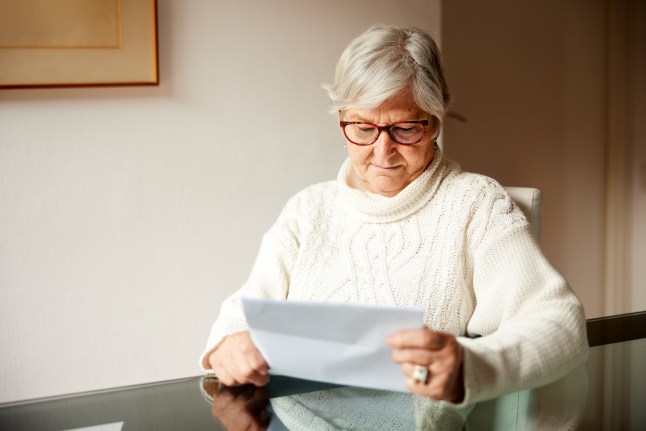 A senior woman sits at the table reading mail.
